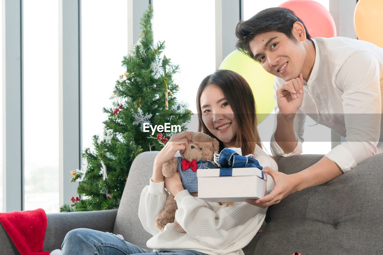 Portrait of smiling young couple holding christmas present at home
