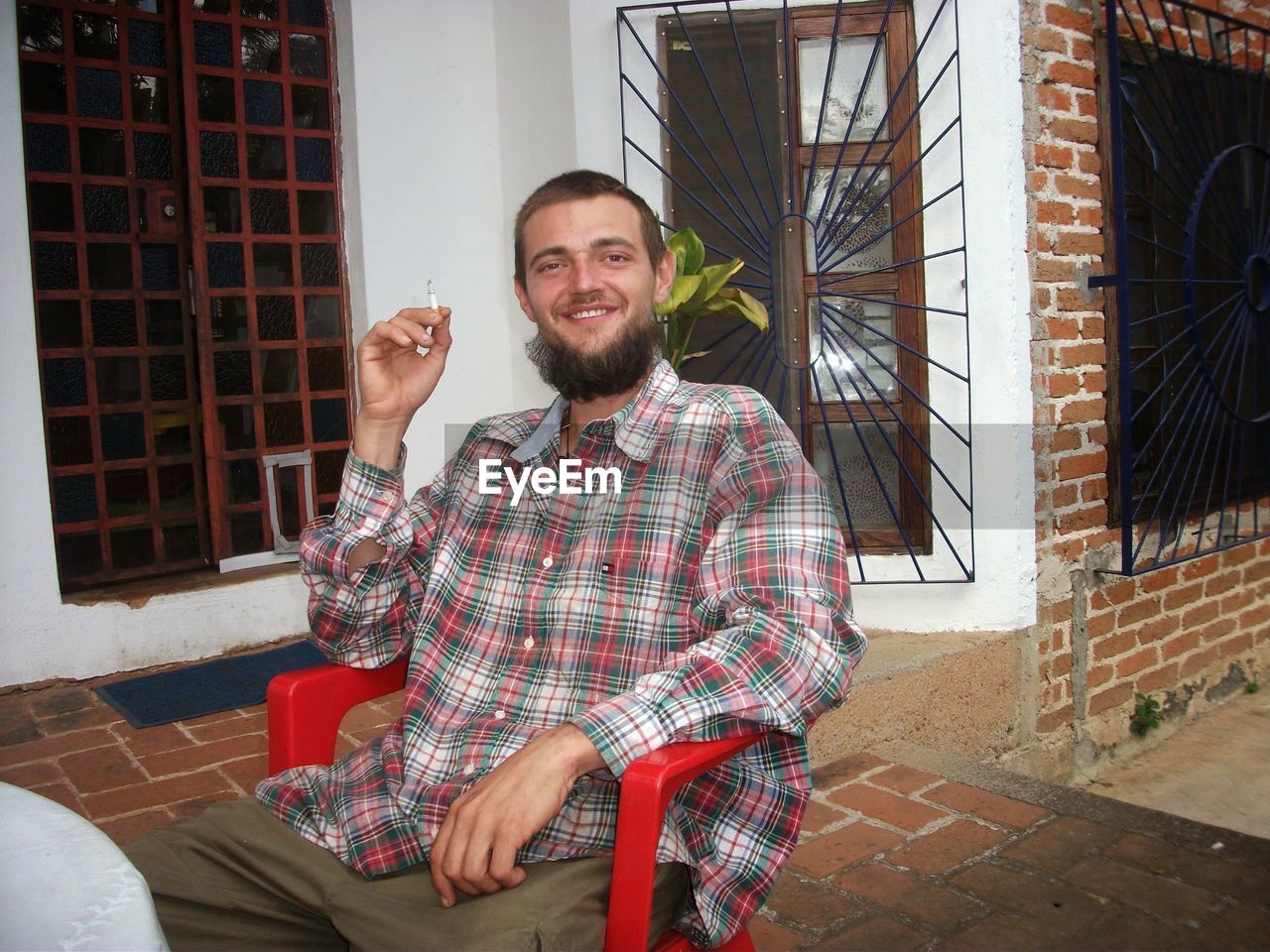 Portrait of smiling young man smoking cigarette on porch