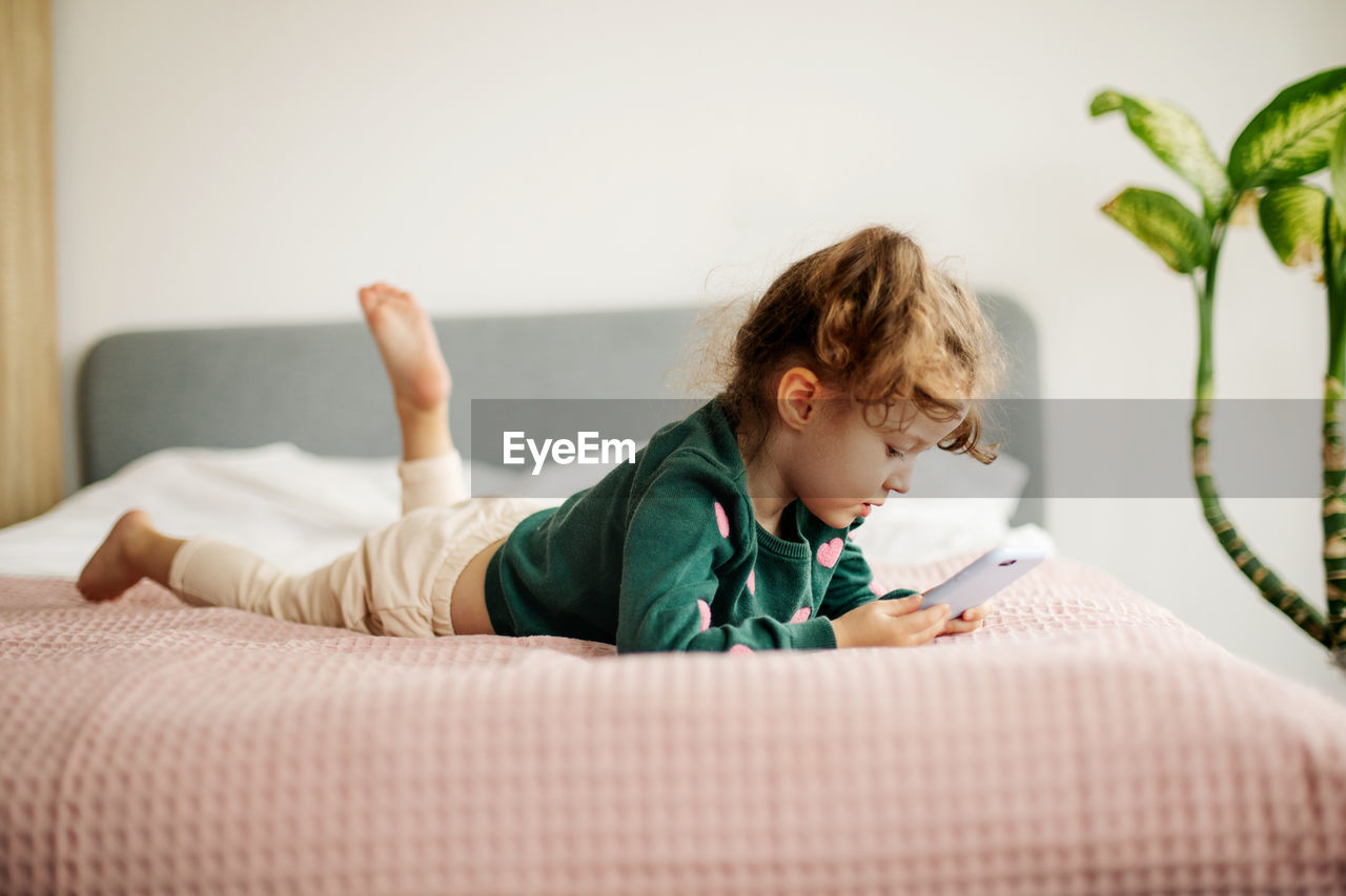 A little girl is happily looking at a smartphone, playing a game or watching cartoons