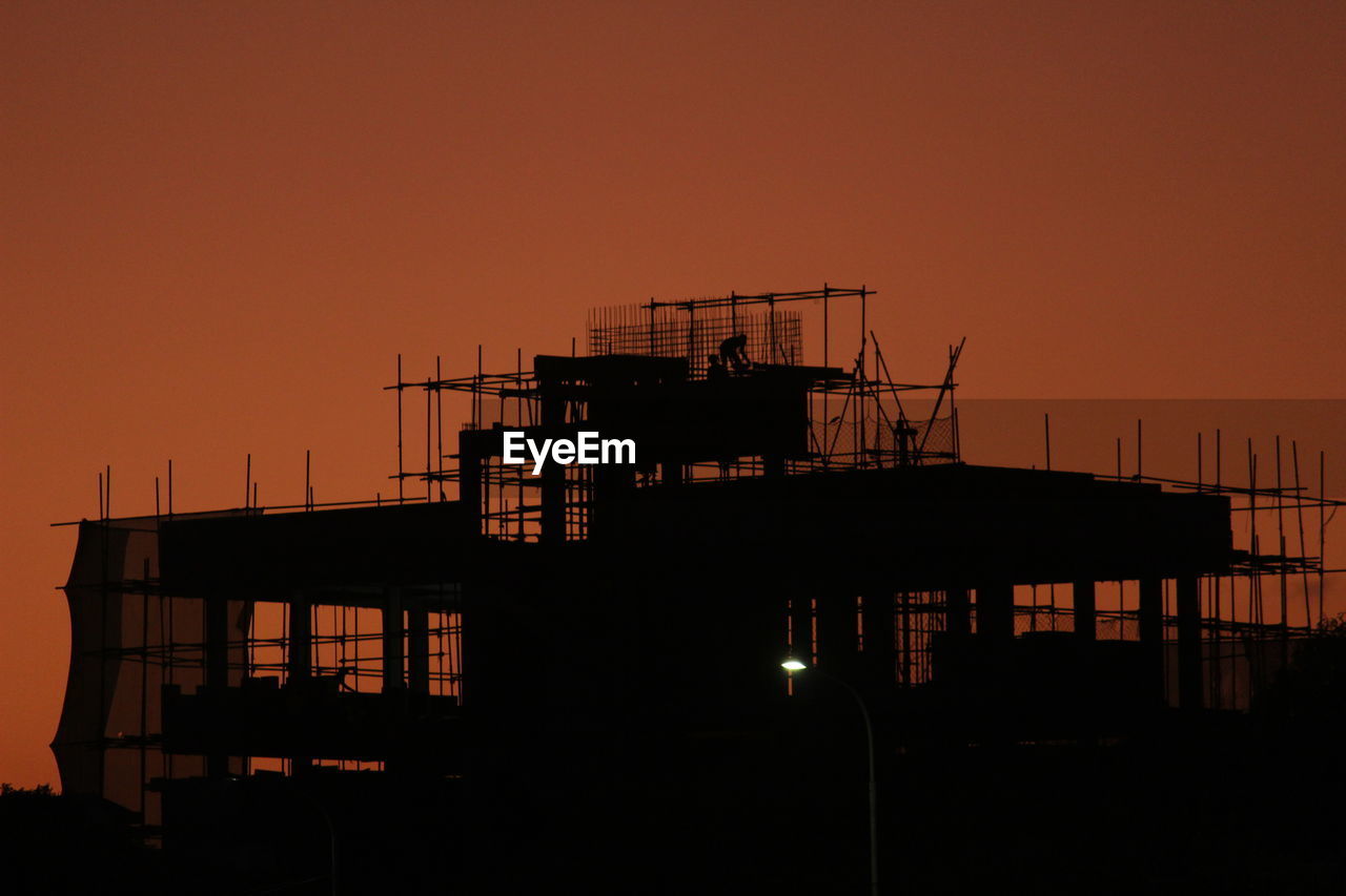 Silhouette built structure by sea against orange sky at sunset