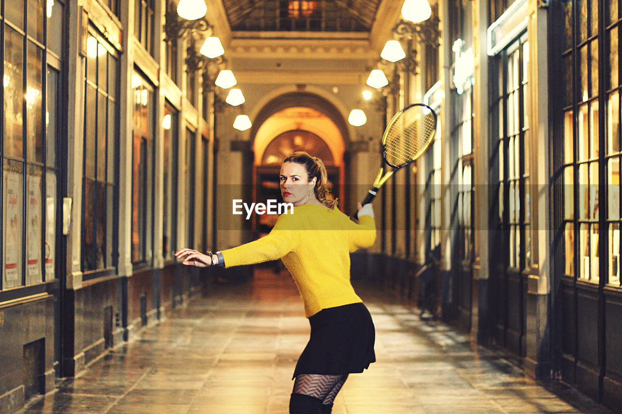 Portrait of woman with badminton racket standing in corridor of building