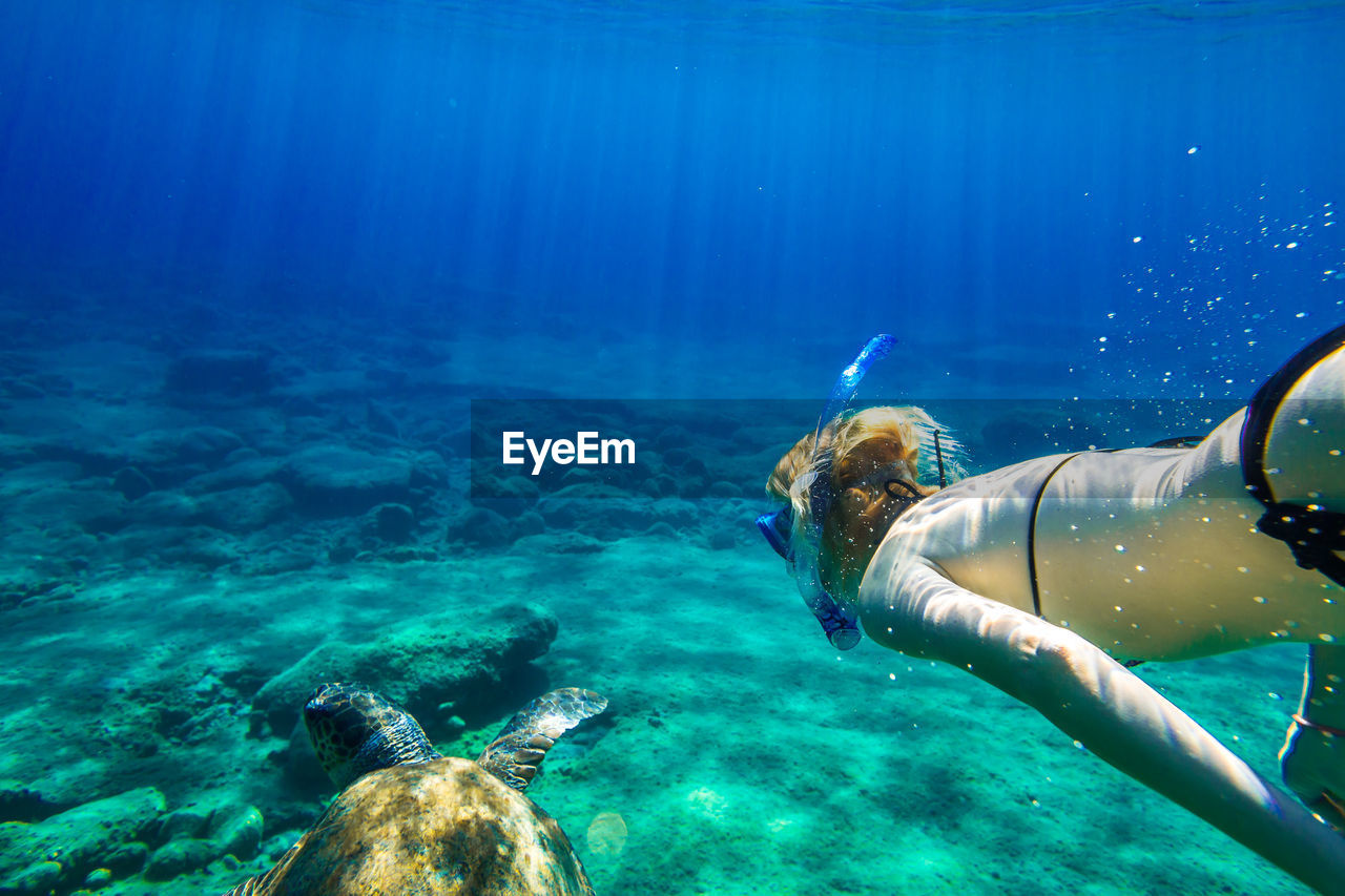 Close-up of mature woman swimming undersea with turtle