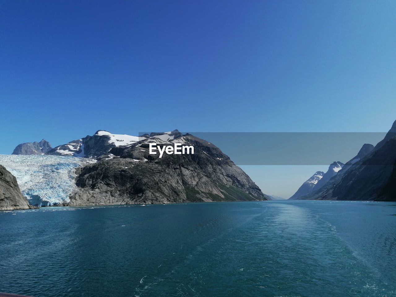 Scenic view of sea and snowcapped mountains against clear blue sky