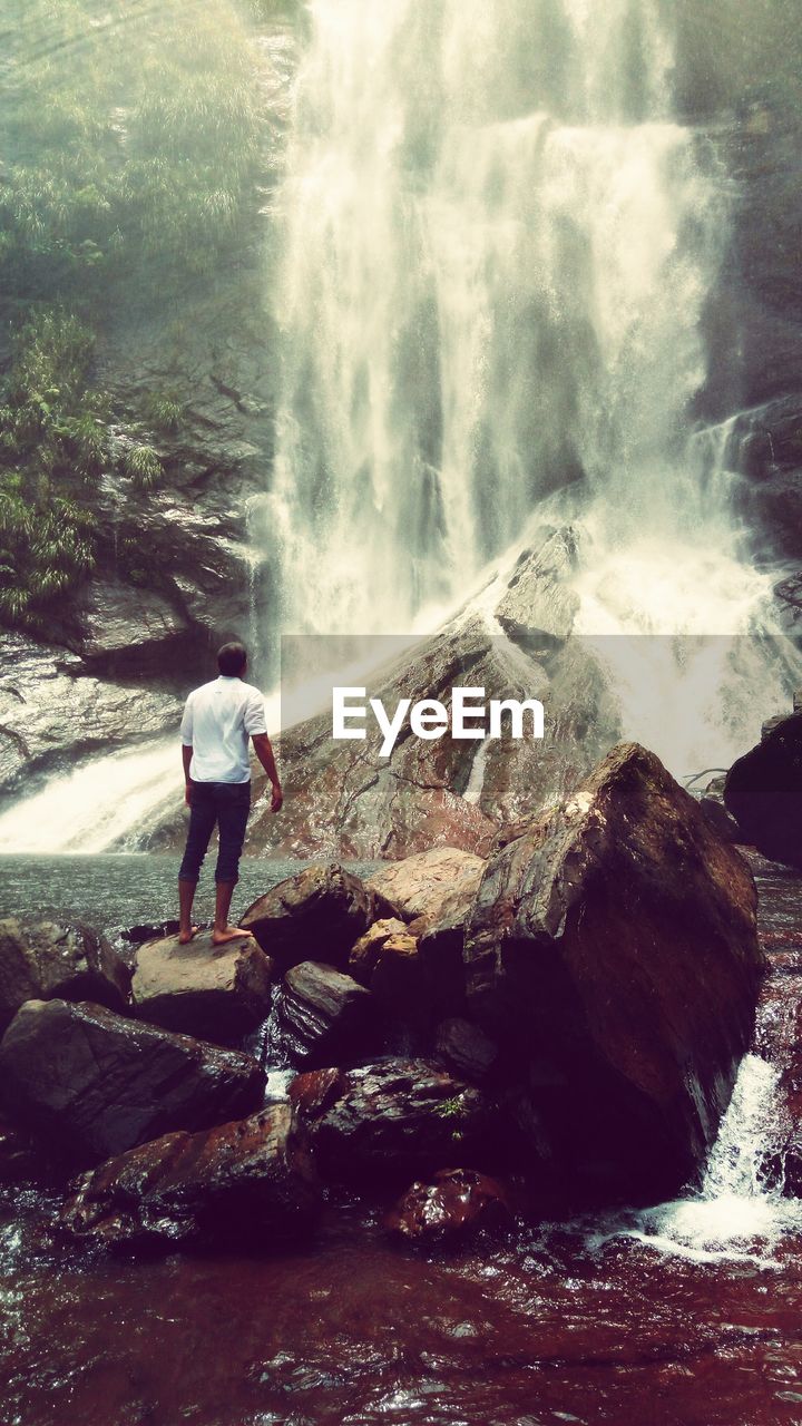 Rear view of man standing against waterfall