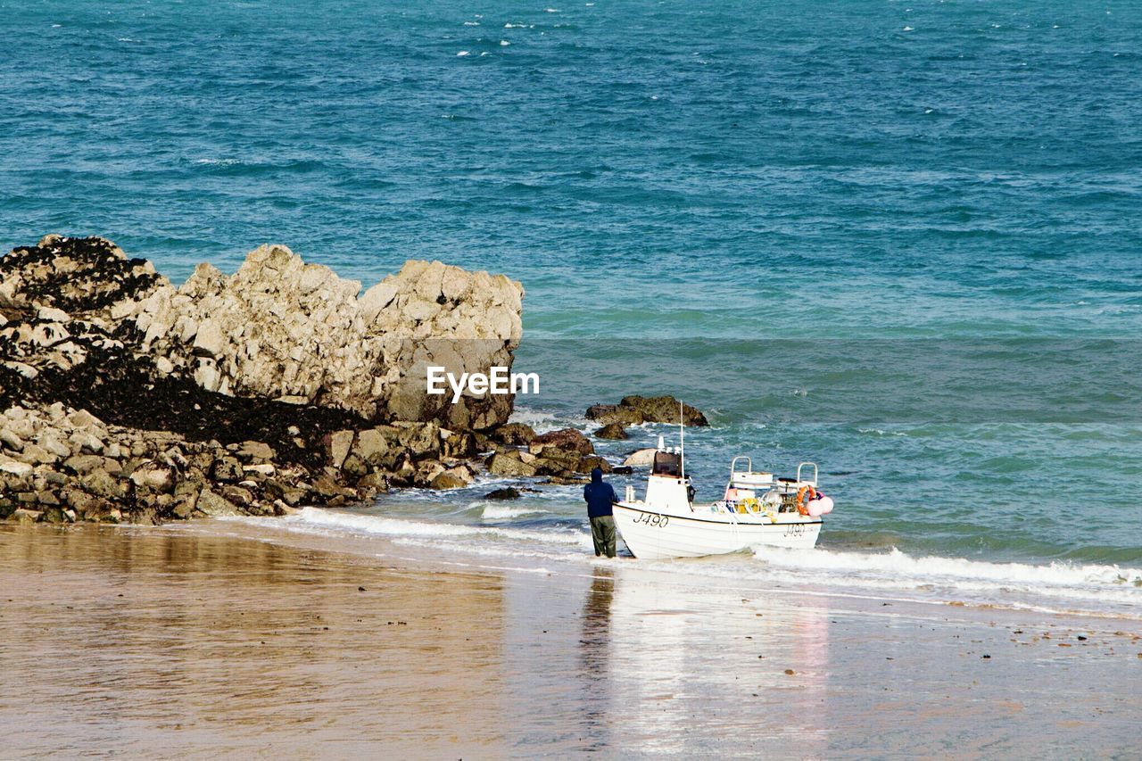 Rear view of man standing by boat moored at beach