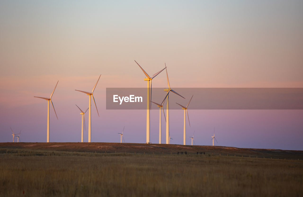 Wind turbines in field against sunset sky