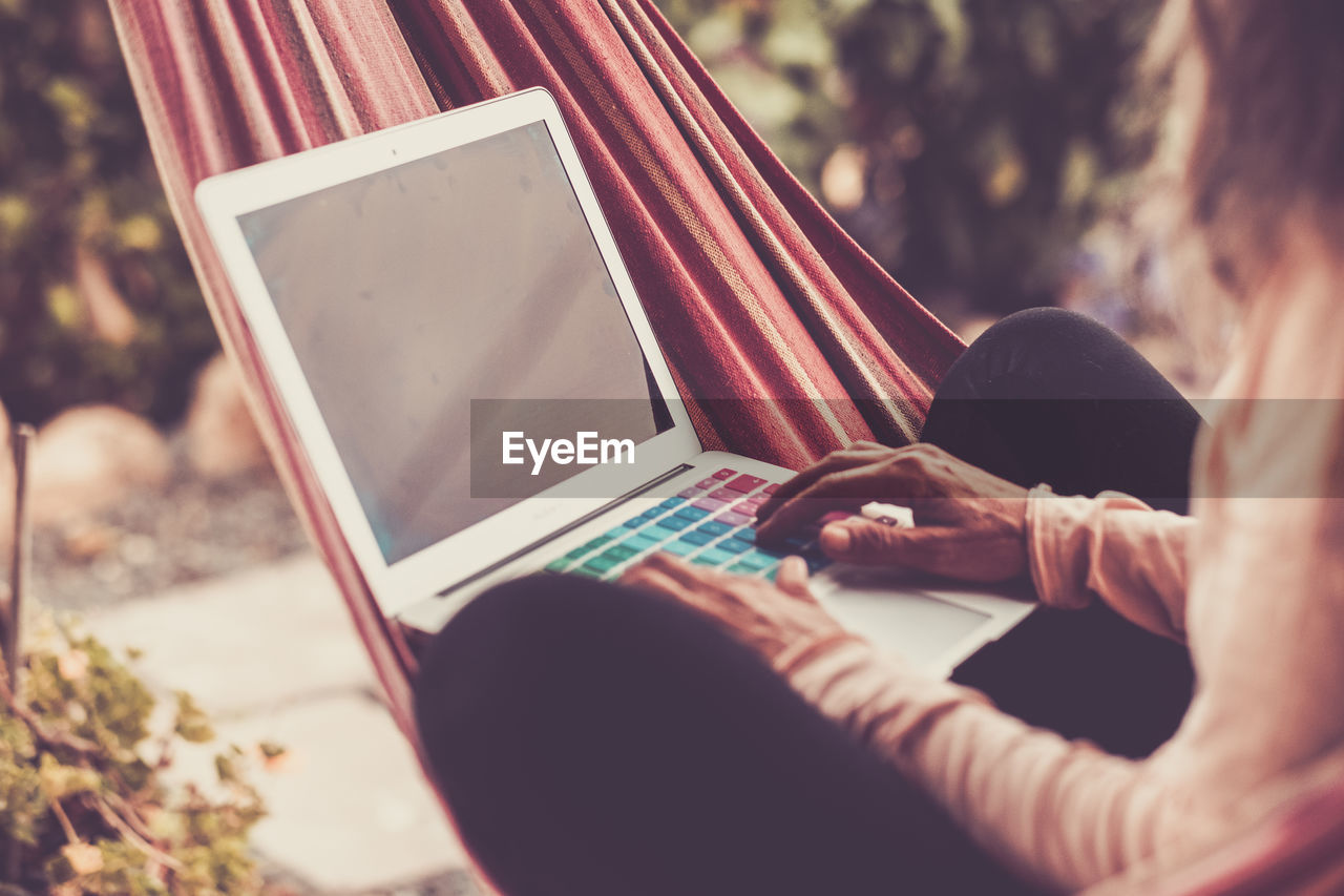 Midsection of woman using laptop while sitting on hammock