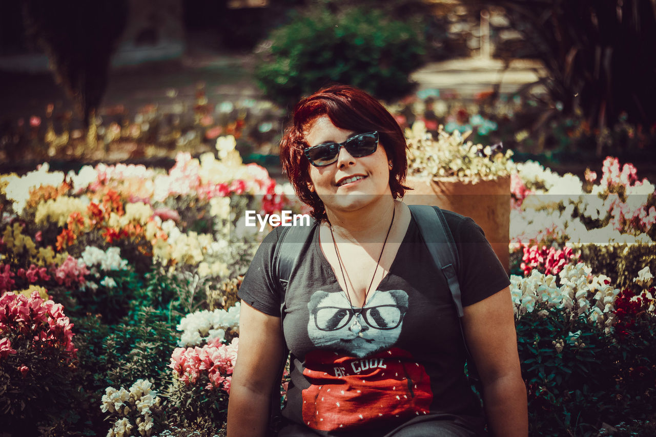 Portrait of smiling woman wearing sunglasses sitting against flowers