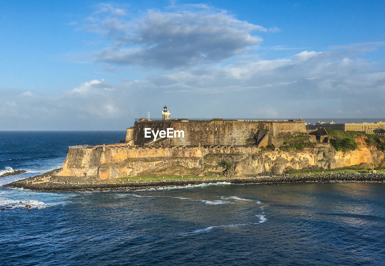 Scenic view of sea and fortress against blue sky surrounded by ocean. 