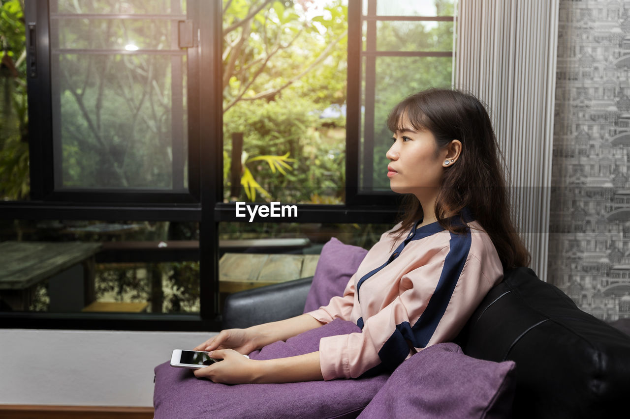 portrait of young woman using mobile phone while sitting at home