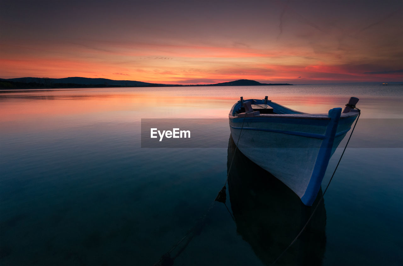 Boat moored on lake against sky during sunset