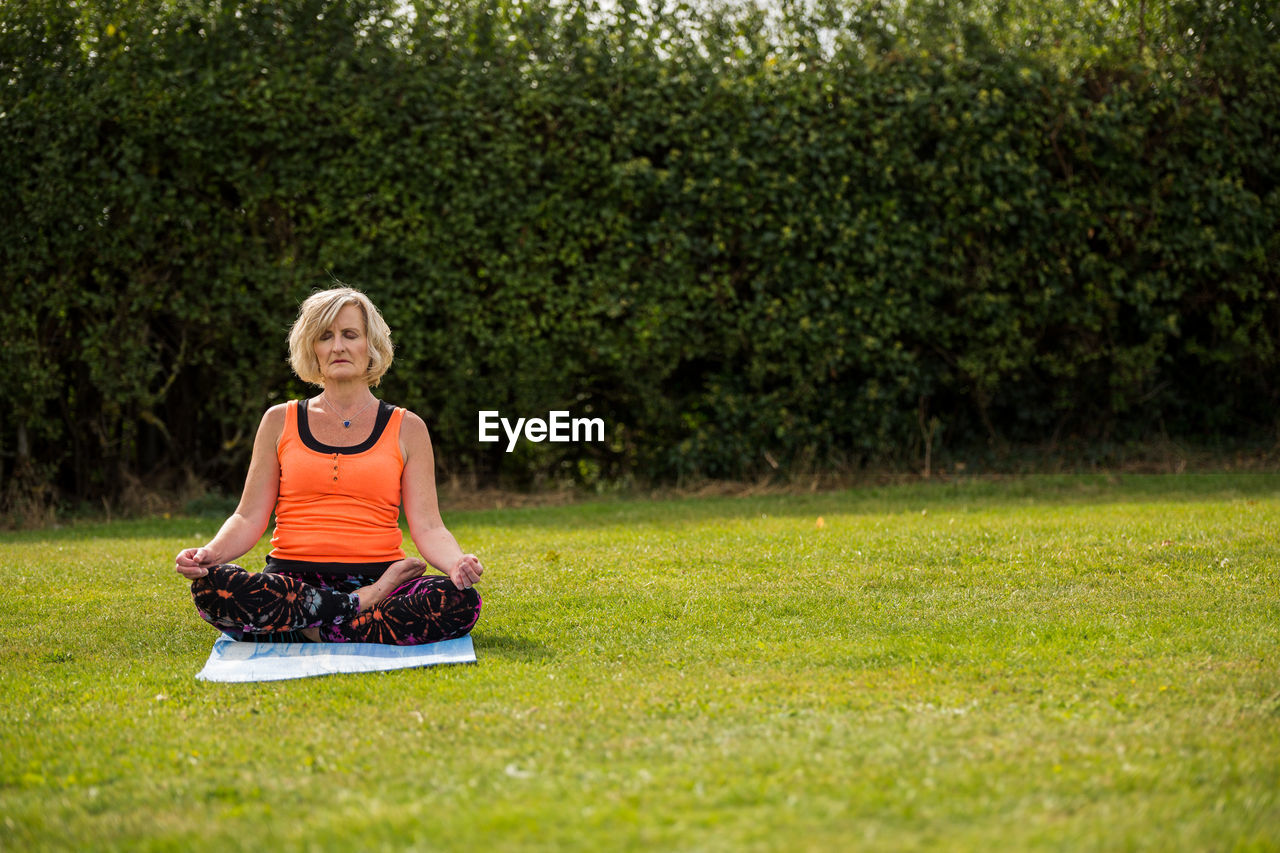 FULL LENGTH OF WOMAN SITTING ON GRASSLAND