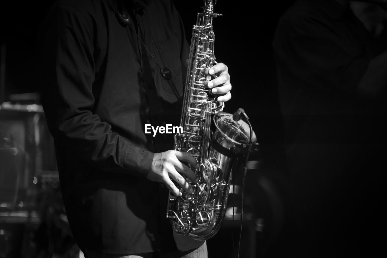 Midsection of man playing saxophone in darkroom