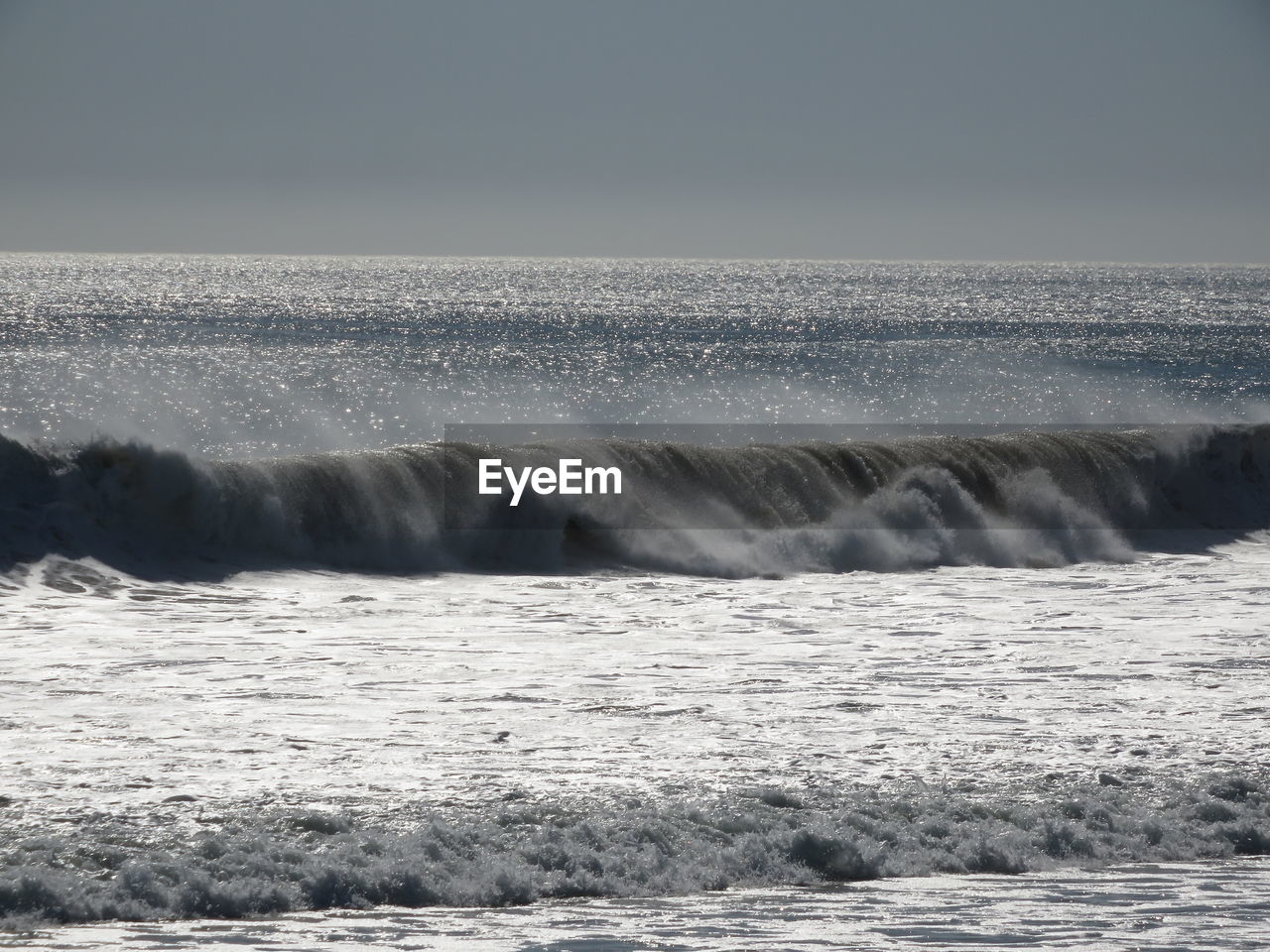 Sea waves splashing on shore against sky