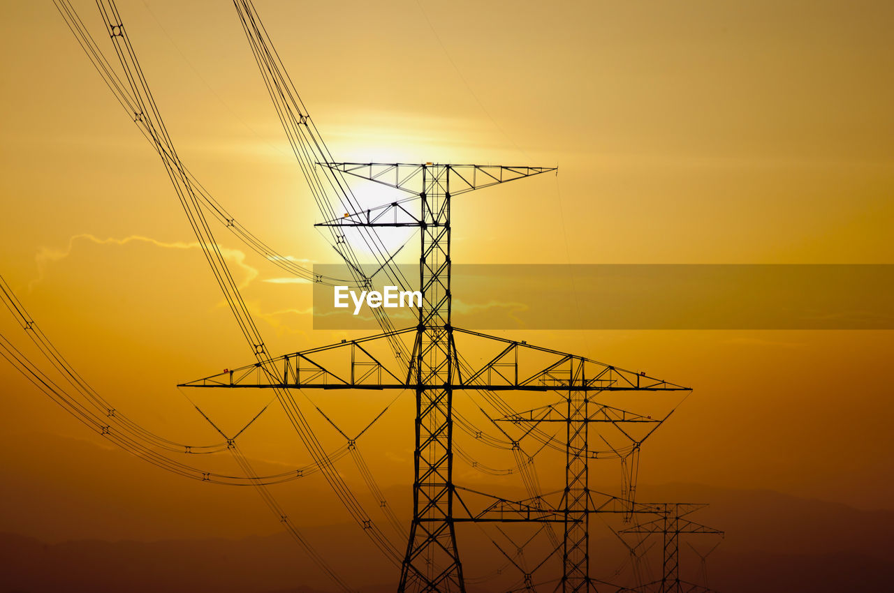 Low angle view of electricity pylon against sky during sunset