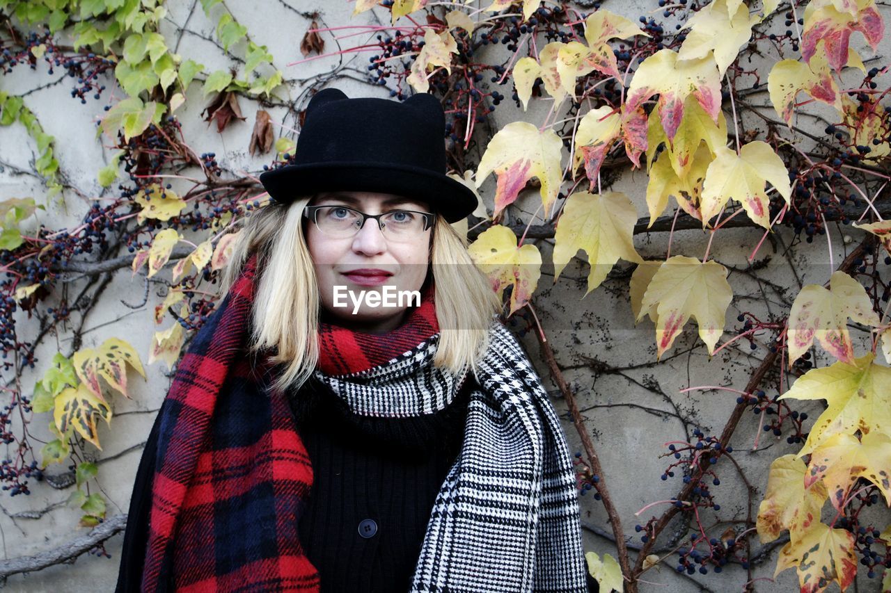 Portrait of mature woman in wearing hat while standing by ivies on wall