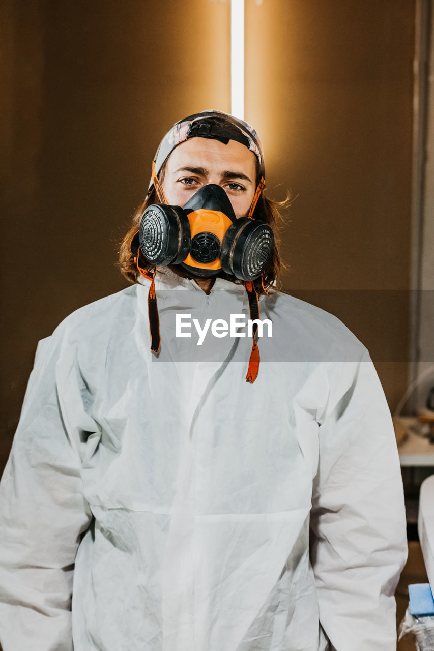 Male worker wearing safety respirator and protective costume in workshop while looking at camera