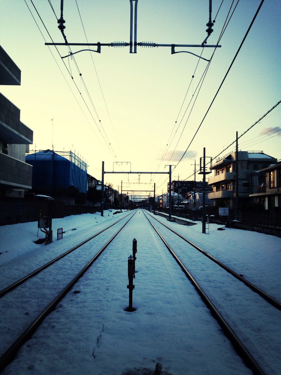 Snow covered railroad tracks against sky in city