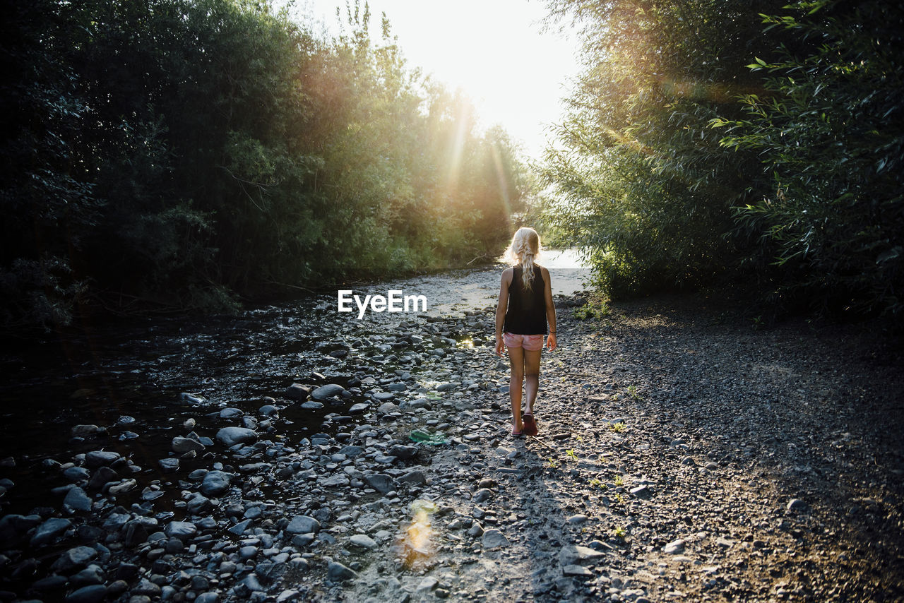 Rear view of carefree girl walking towards river in forest