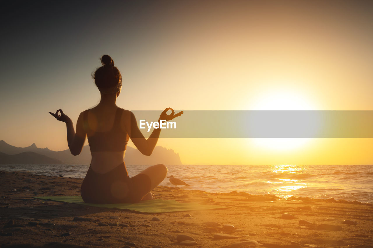 Yoga woman meditating at serene sunset or sunrise on the beach. the girl relaxes in the lotus