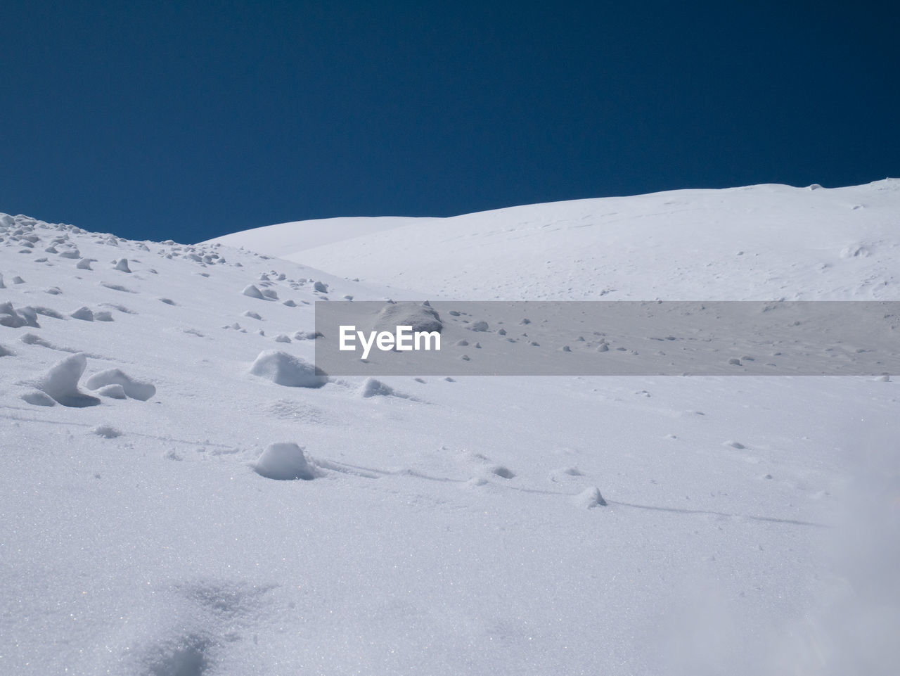 Snow covered landscape against clear blue sky