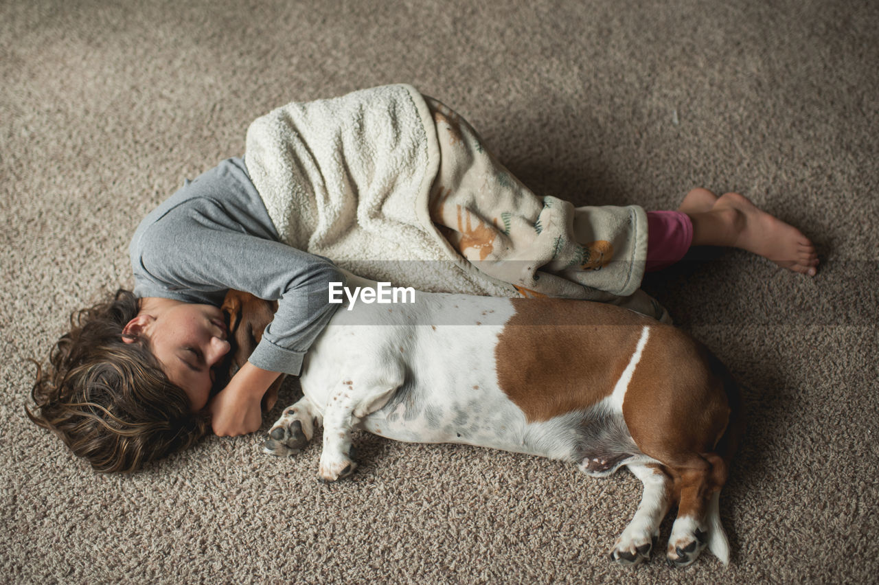 Young girl laying on the floor in blanket with basset hound dog
