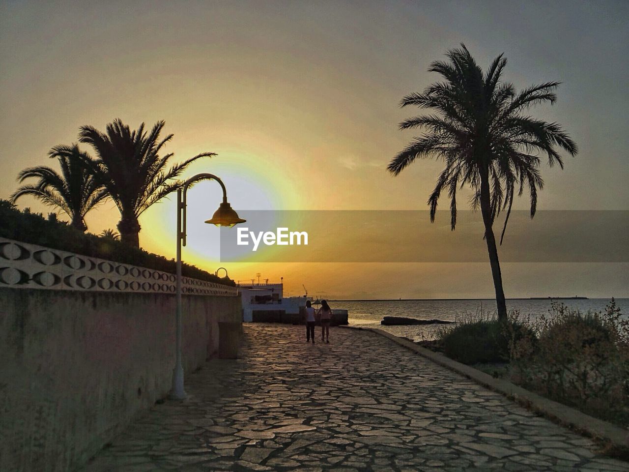 Empty walkway leading to calm sea at sunset