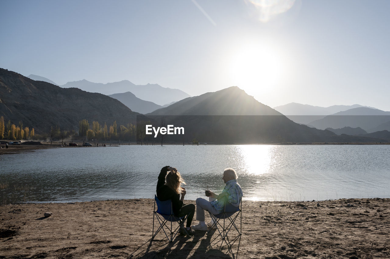 Senior man and his daughter relaxing together sitting outdoors near a lake in nature.