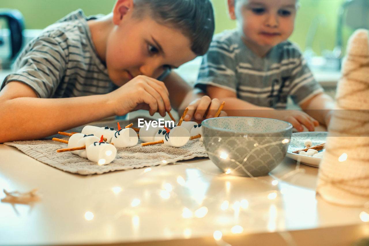 Cute brothers decorating marshmallows at home