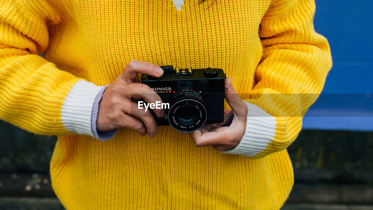 MIDSECTION OF WOMAN HOLDING CAMERA