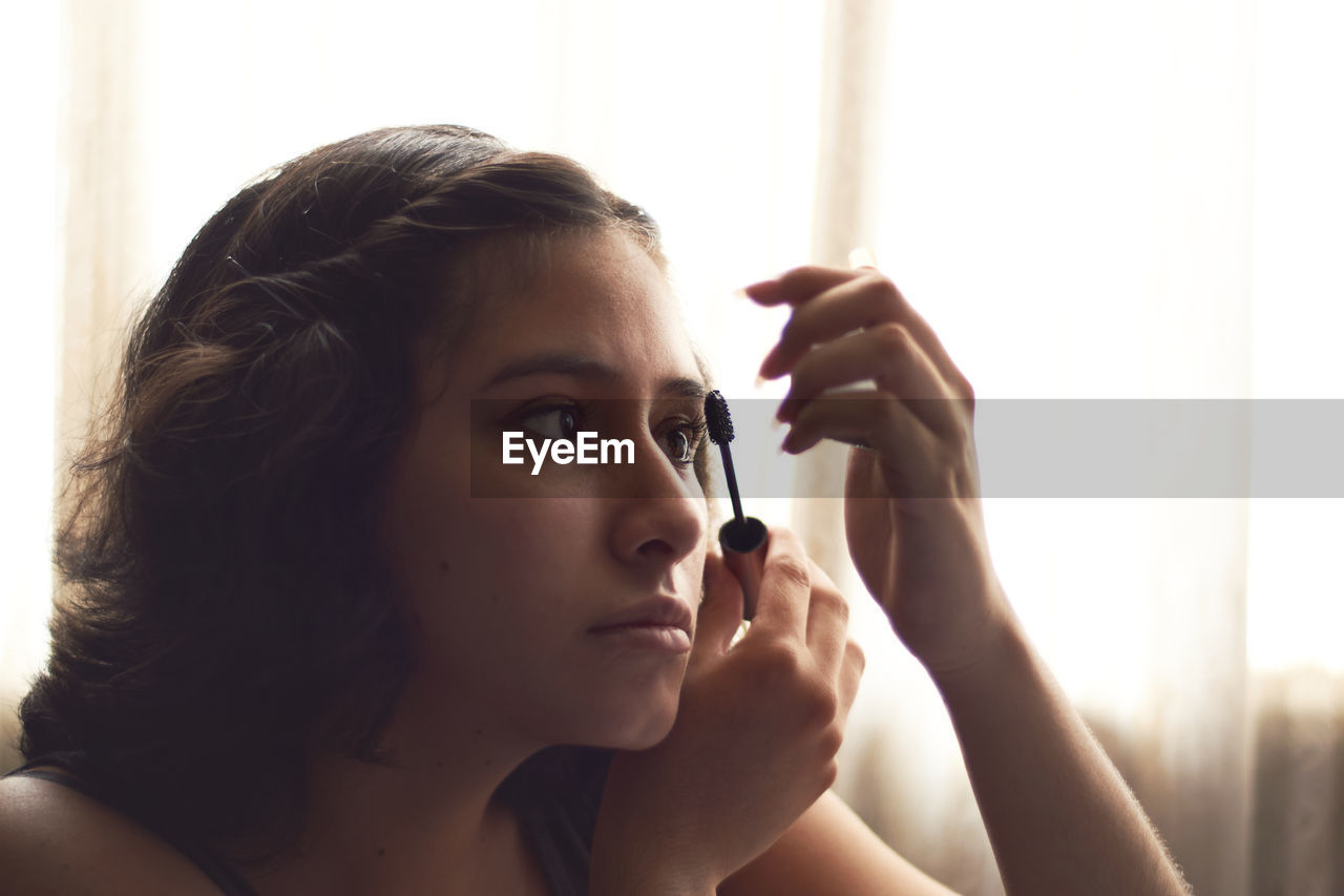 Portrait of young woman putting on makeup, with sun behind