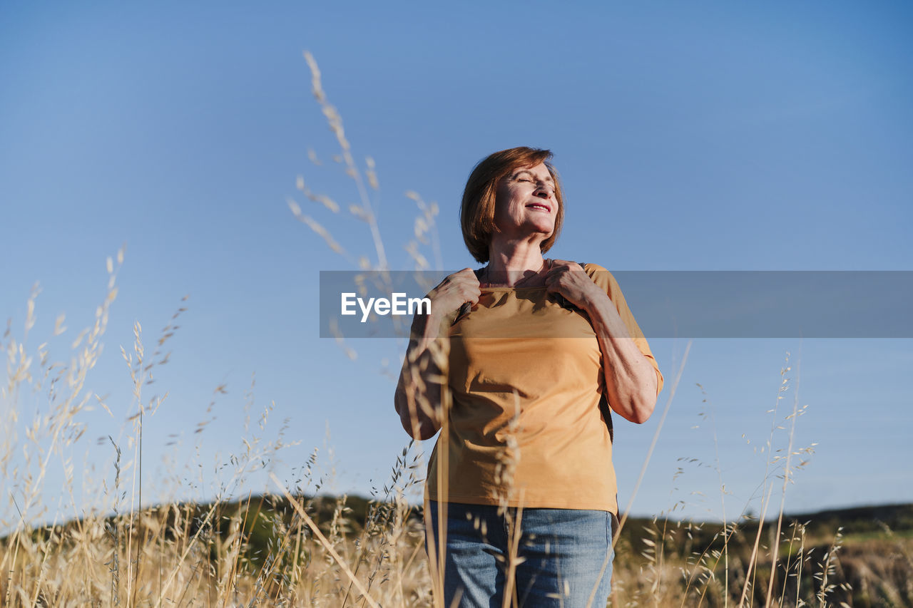 Smiling senior woman with eyes closed hiking on sunny day