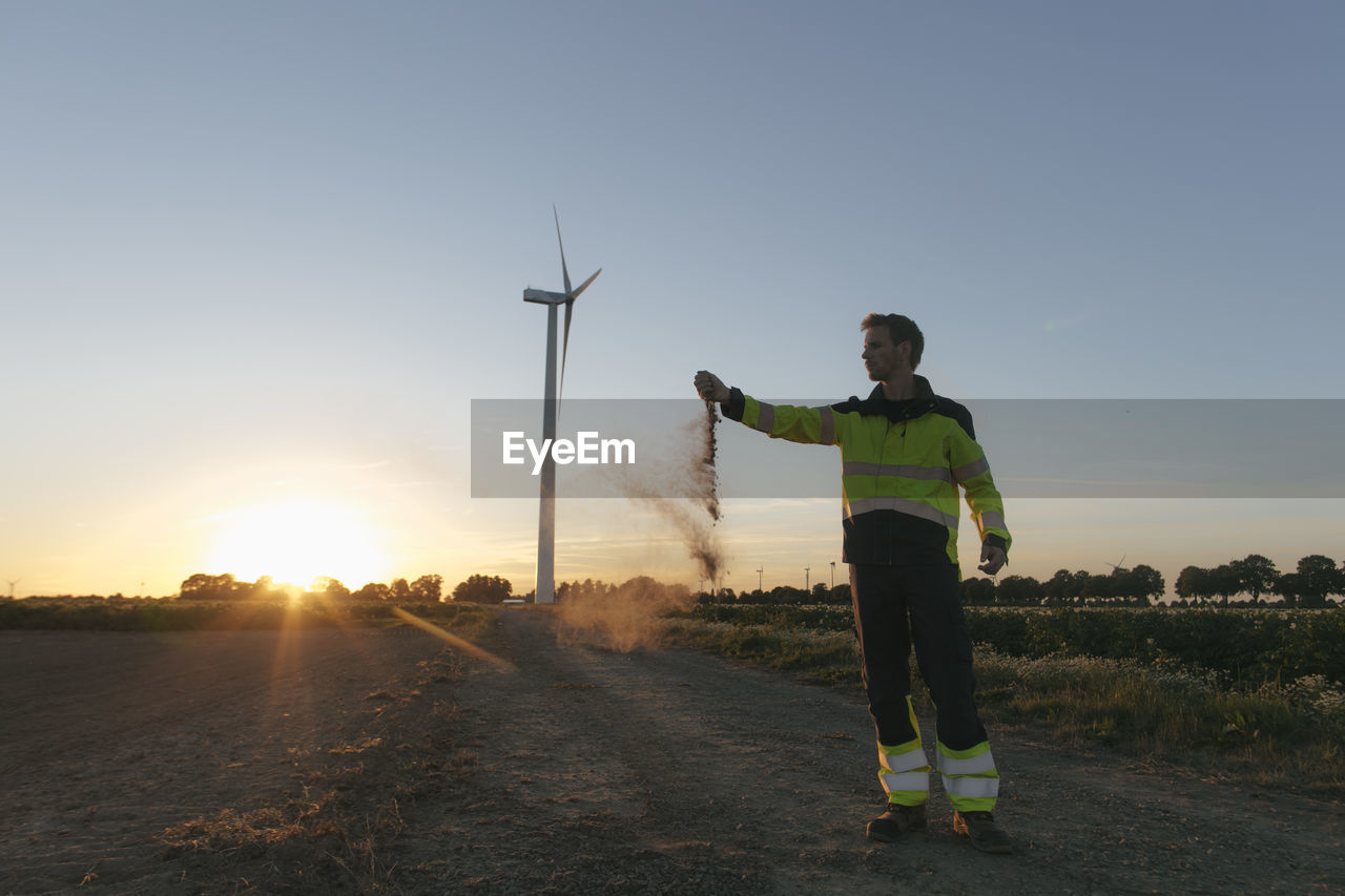 Engineer at a wind turbine at sunset scattering soil