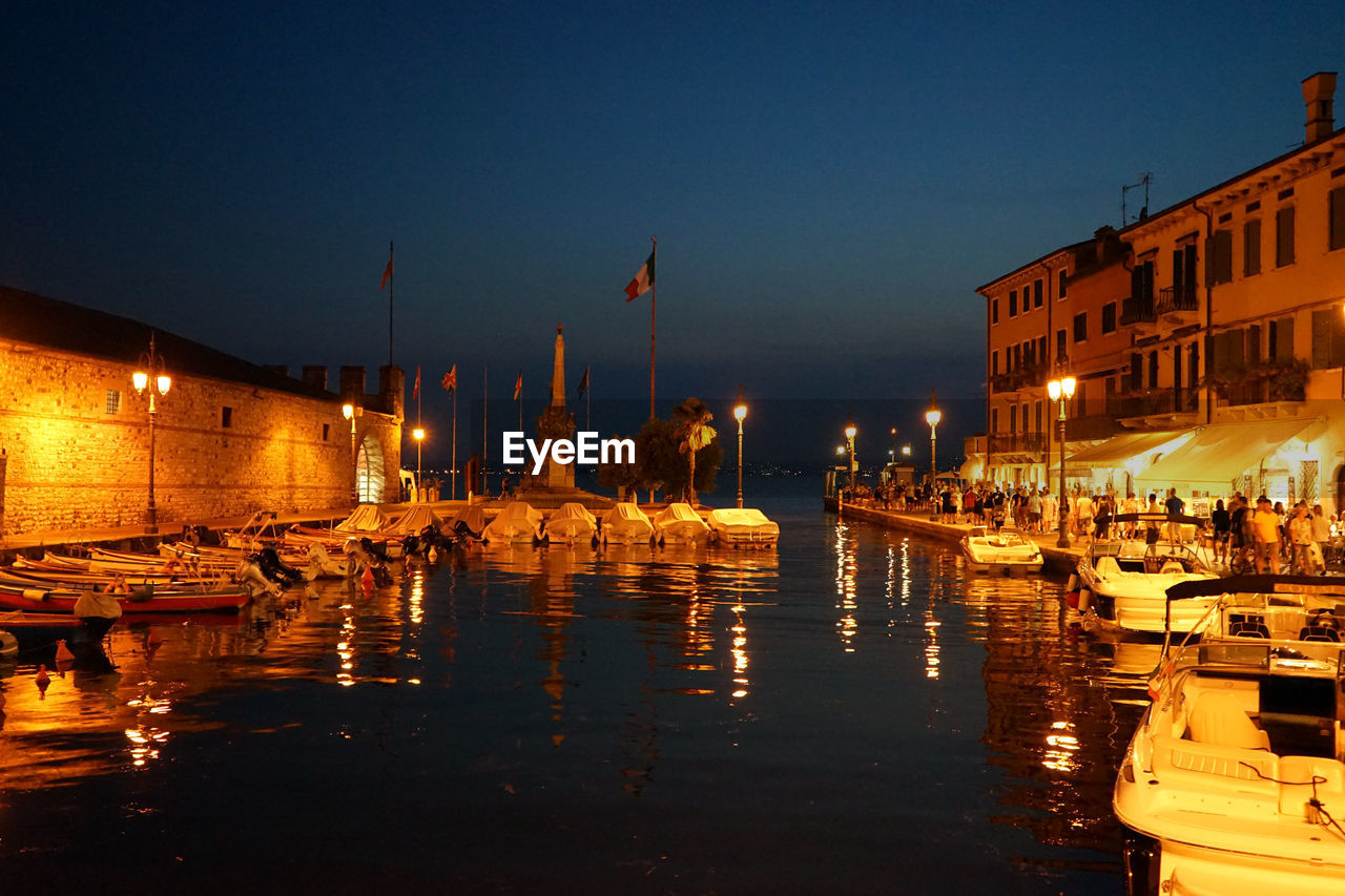 SAILBOATS MOORED IN ILLUMINATED CITY BUILDINGS AT NIGHT