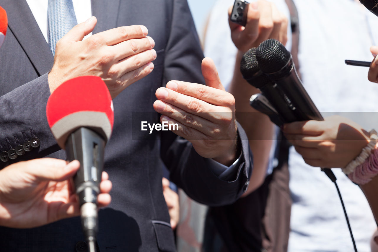 Midsection of businessman giving interview to journalists