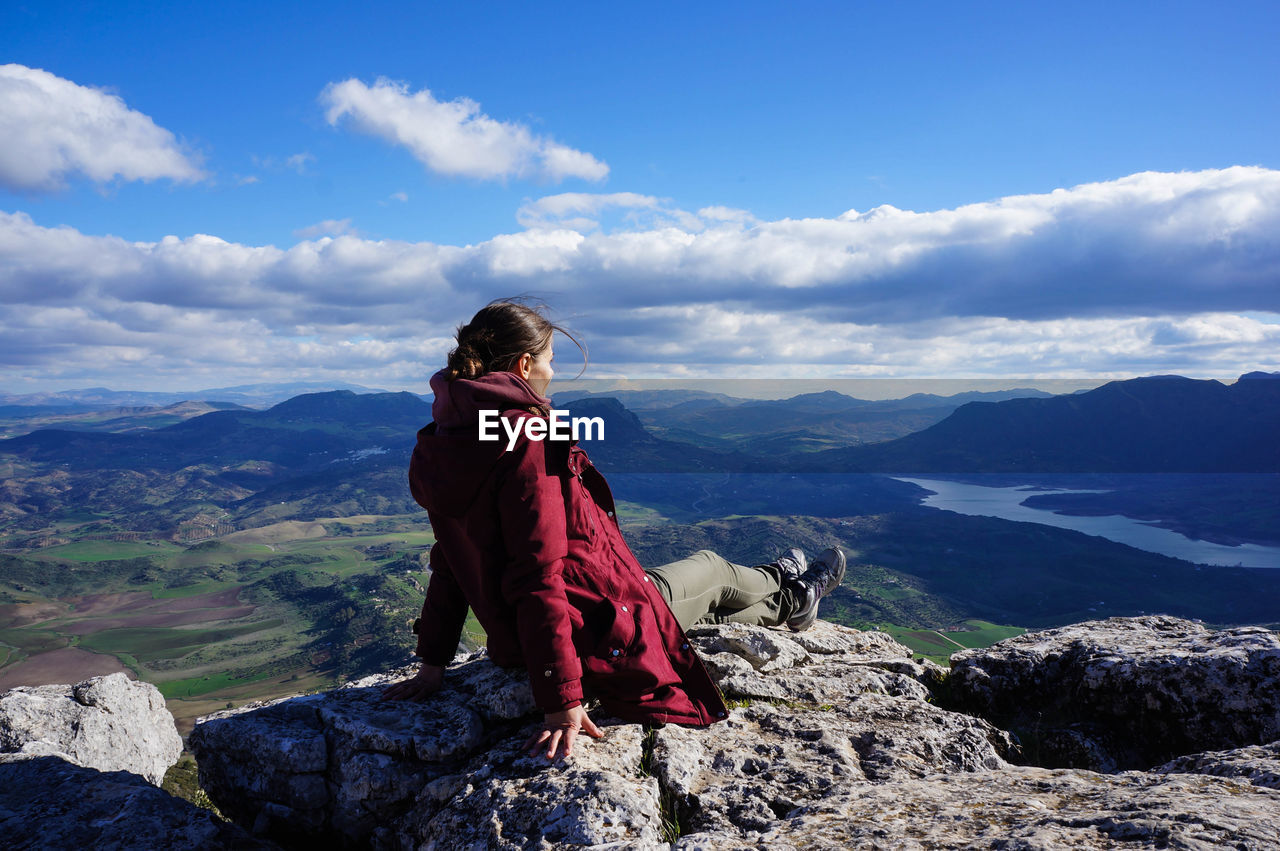 Mid adult woman sitting on cliff against cloudy sky