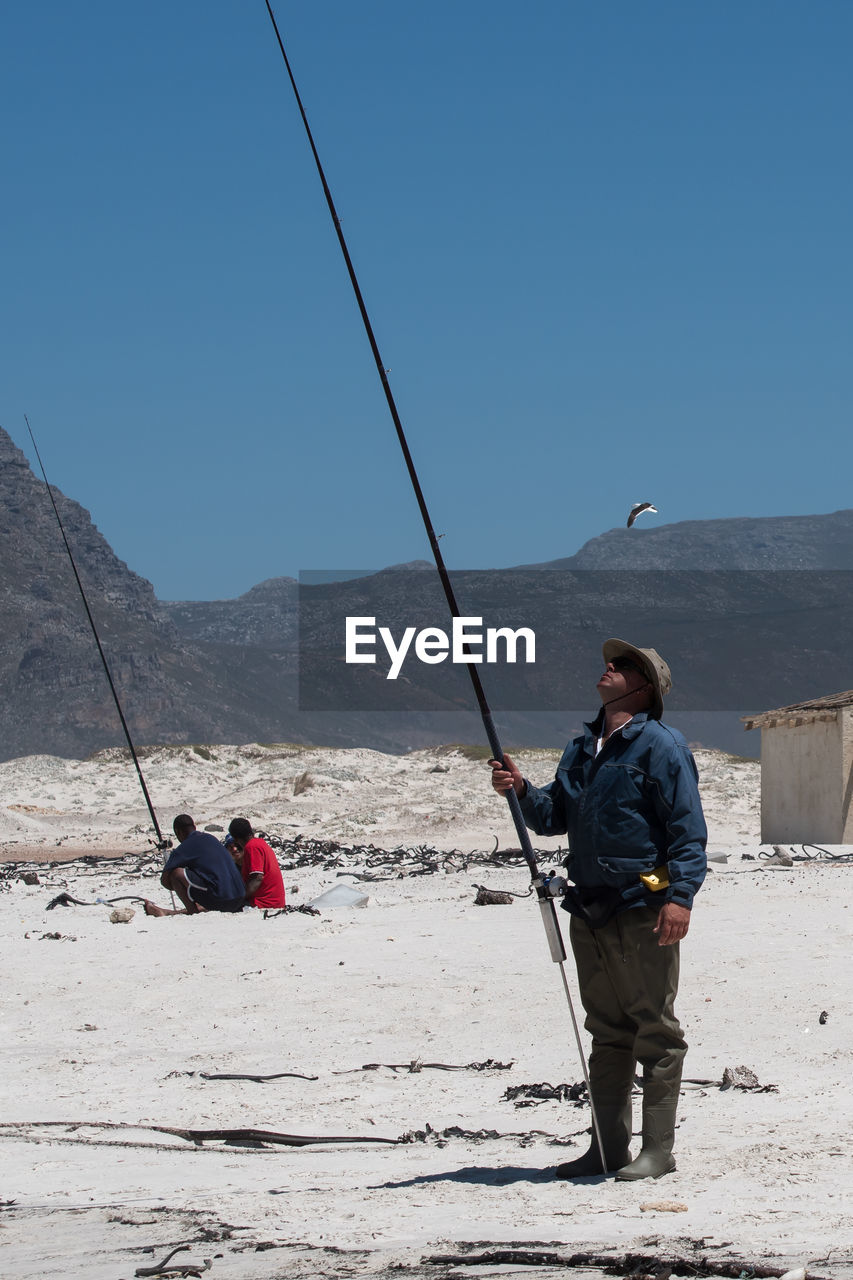 MEN FISHING ON MOUNTAIN AGAINST SKY