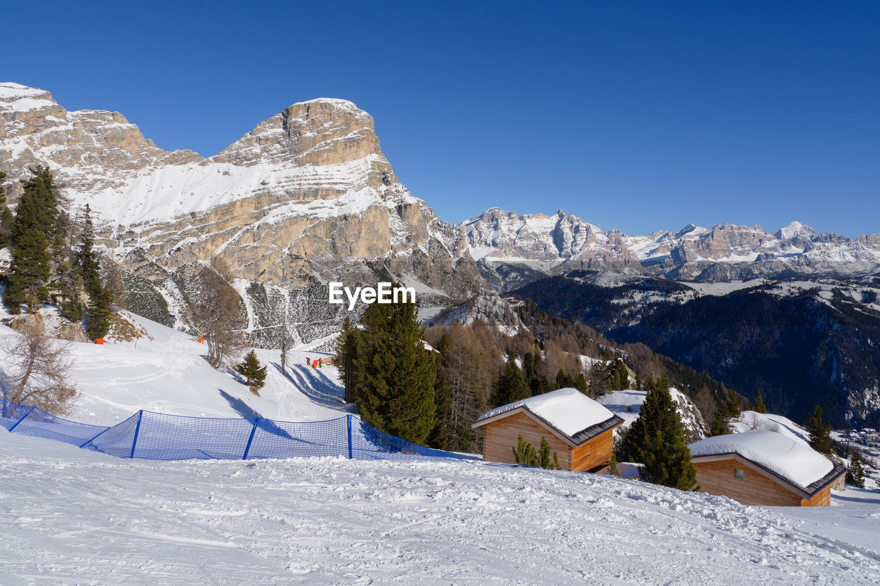 Mountain houses with snow on their roofs and fir trees full of snow, italian alps in the background.