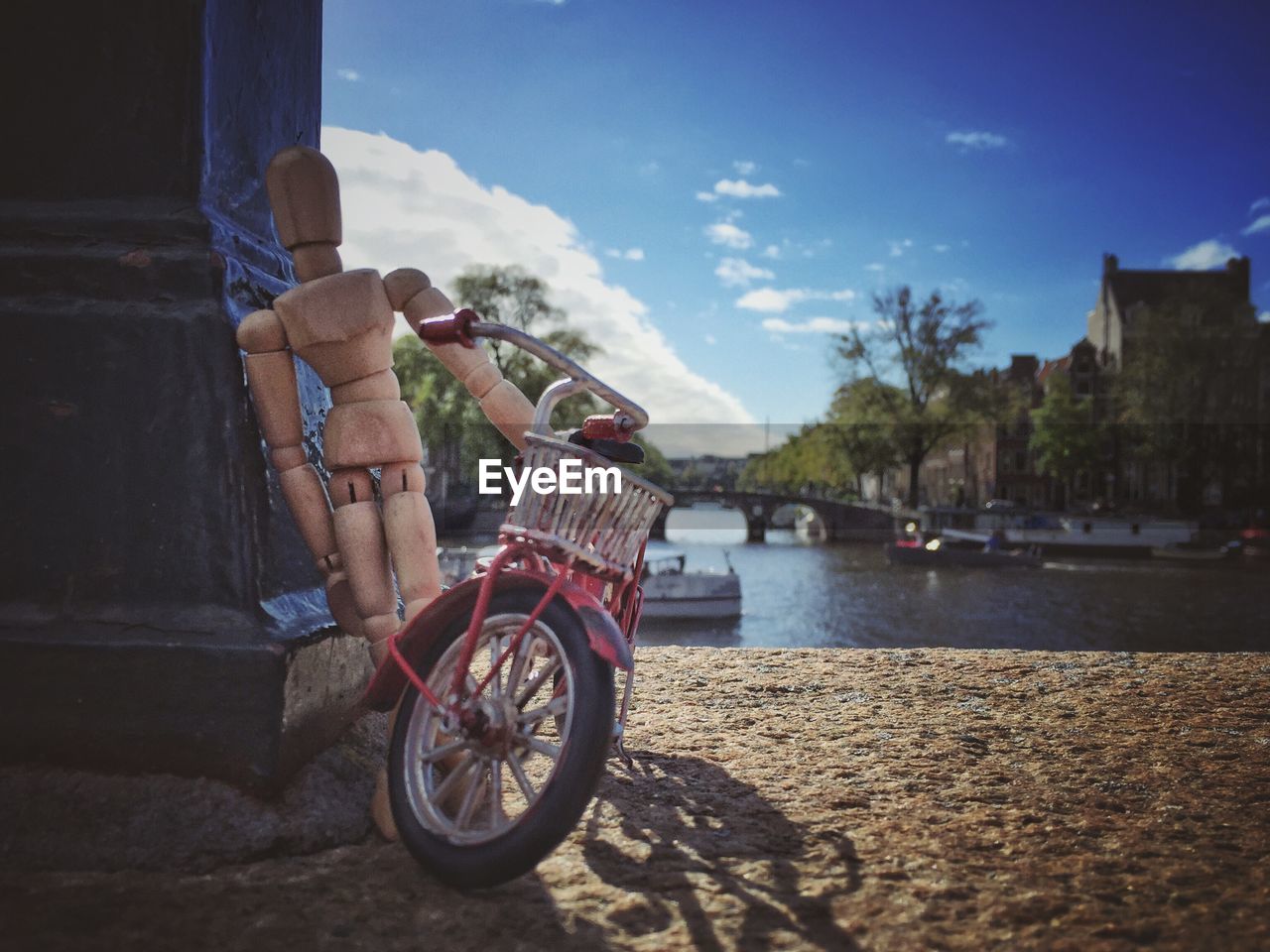 Figurine and toy bicycle by river against sky in city