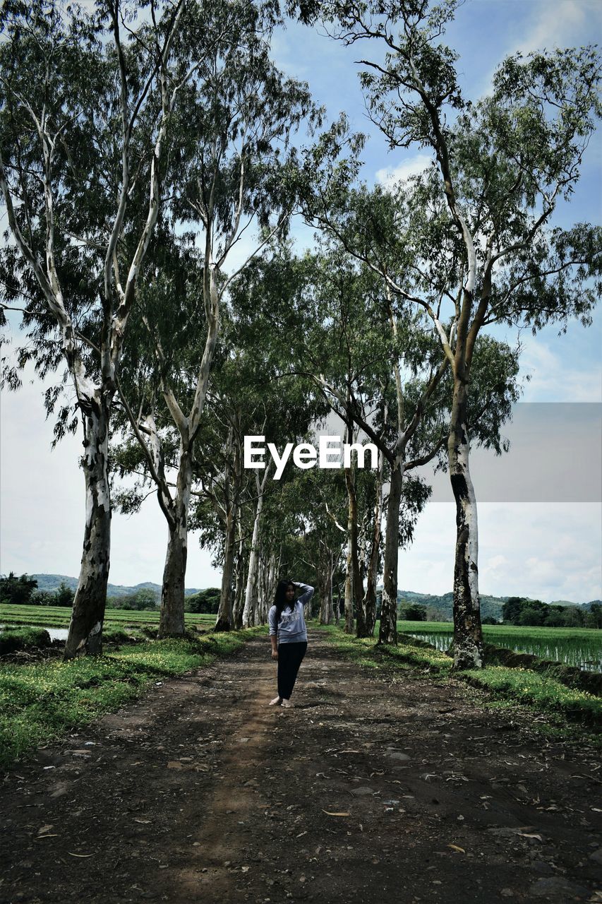 Woman standing on dirt road amidst trees