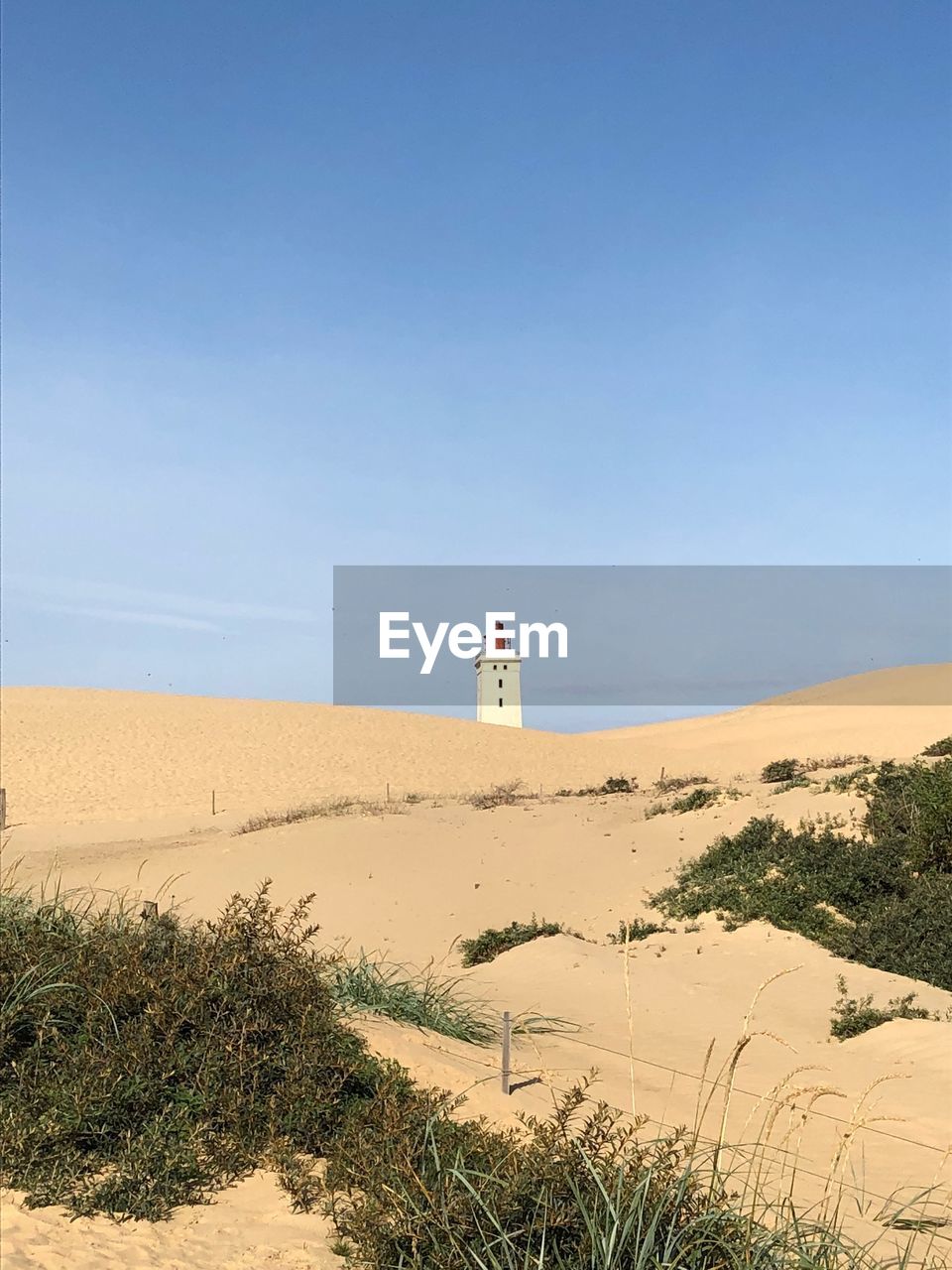 Lighthouse on sand dune against sky