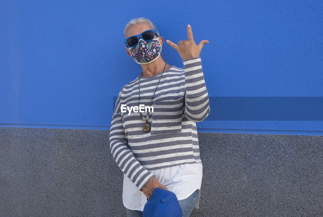 Woman wearing sunglasses standing against blue wall