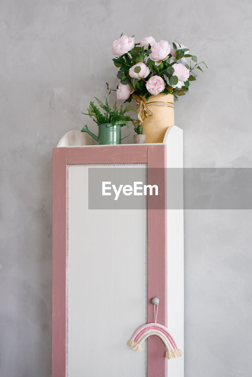 A pencil case cabinet in the children's room with flowers in a vase on it and a watering can