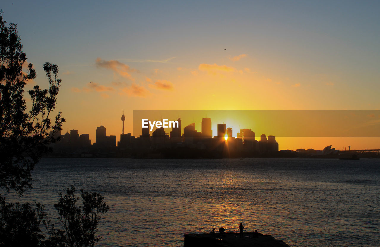 Silhouette city by sea against sky during sunset