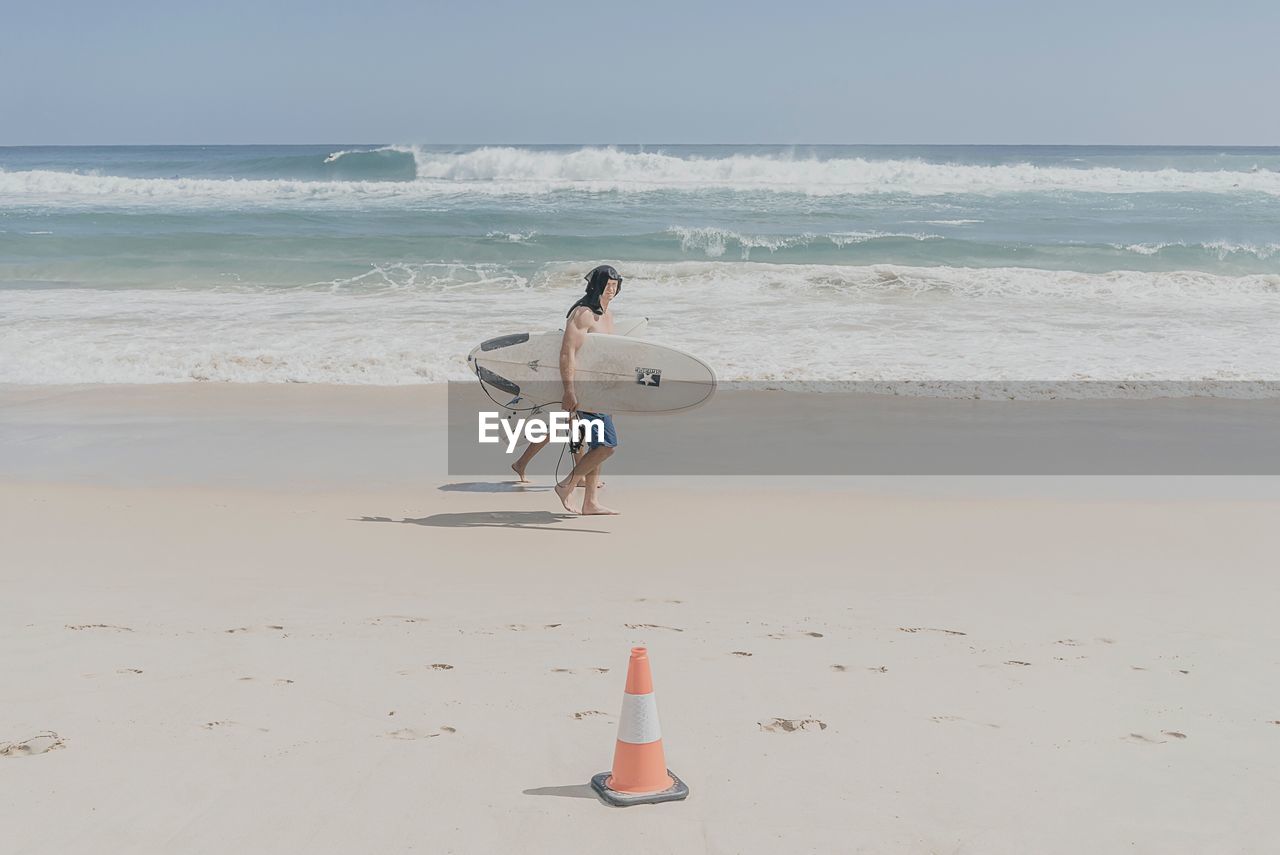 REAR VIEW OF MAN STANDING AT BEACH AGAINST SKY