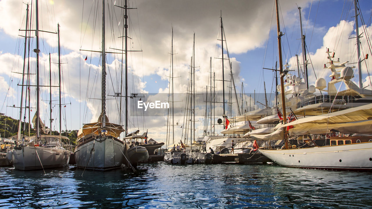 Boats moored at harbor against cloudy sky