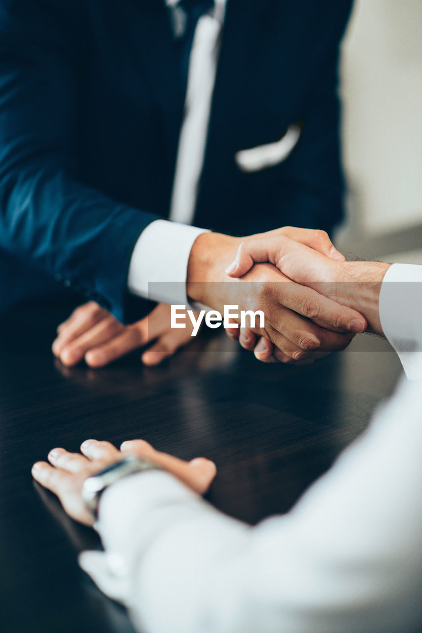 Midsection of business people giving handshake at desk in office