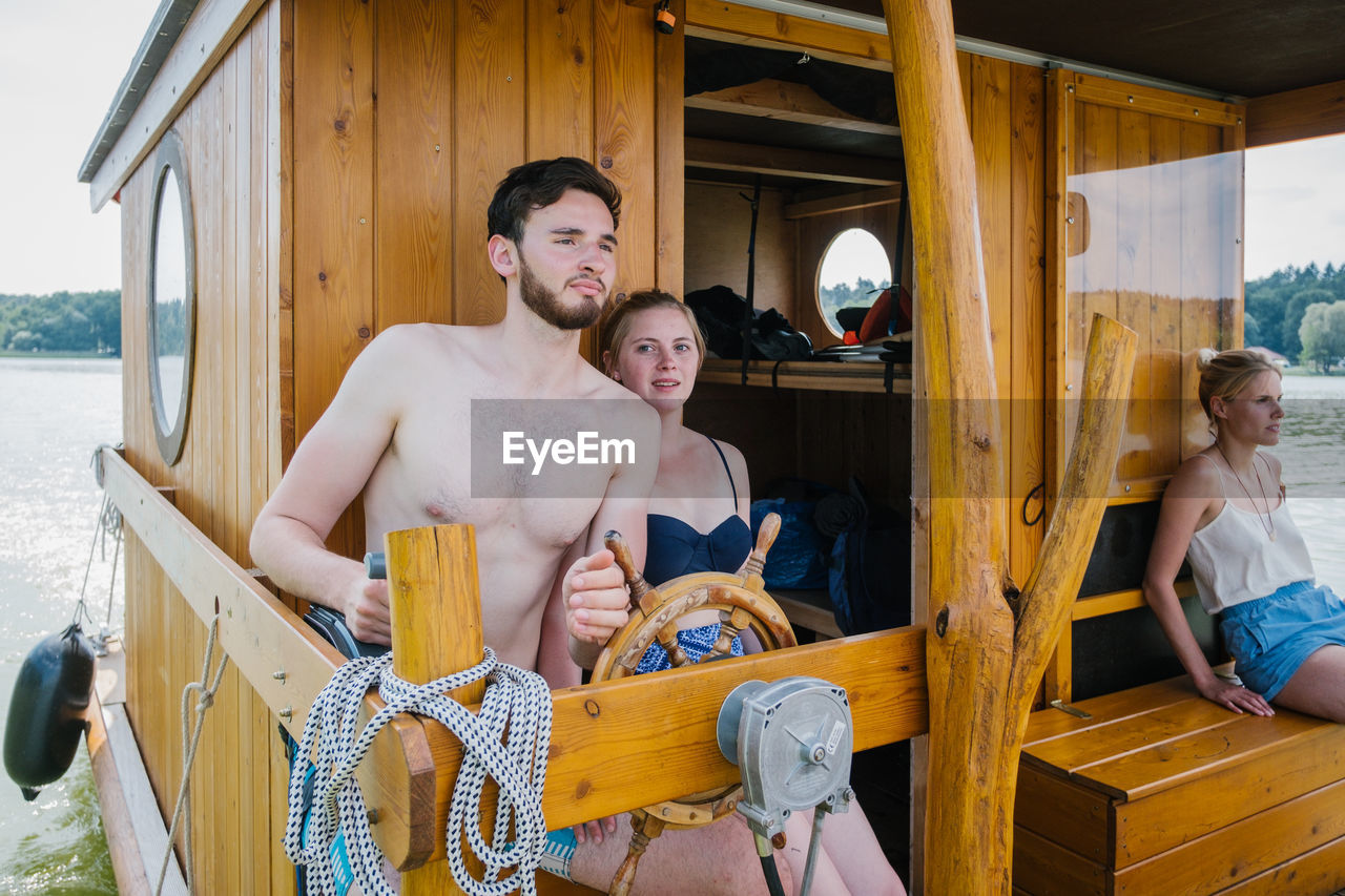 Shirtless man with woman sailing boat in lake