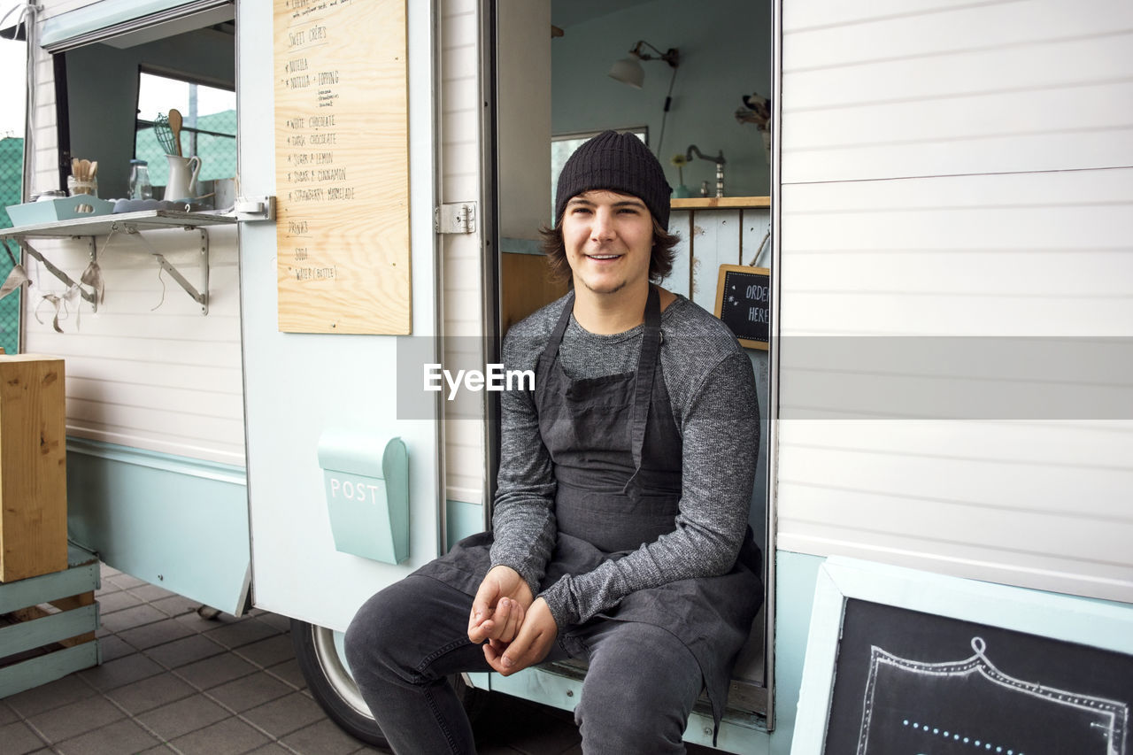Portrait of smiling male owner sitting in food truck on street