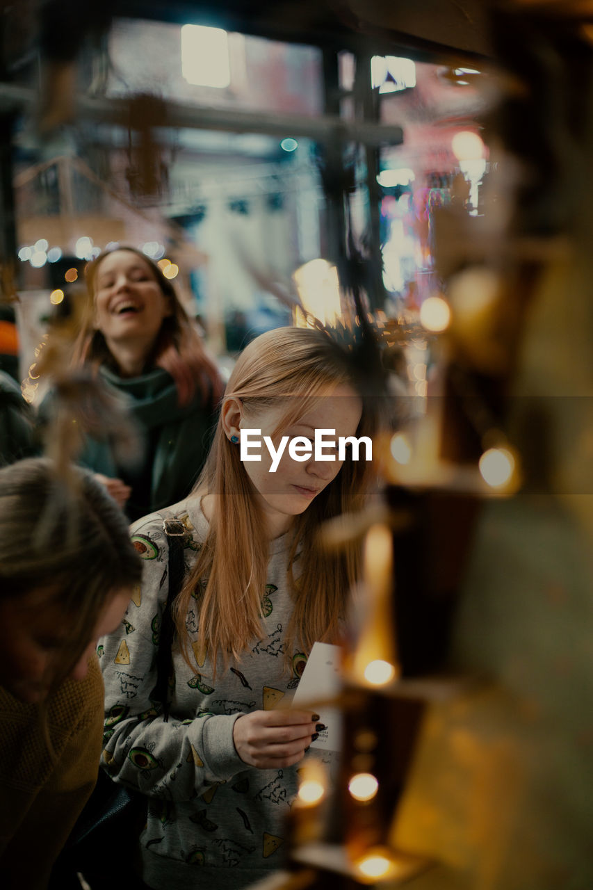 PORTRAIT OF YOUNG WOMAN LOOKING DOWN IN ILLUMINATED SHOP